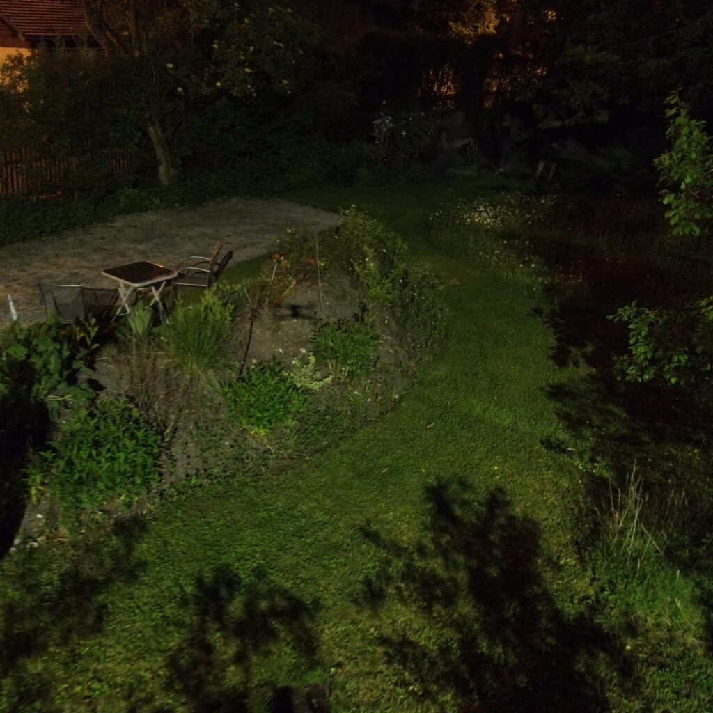 Garten mit Tisch und Stühlen, die von der Straßenbeleuchtung mit grellem. ungemütlichem Licht bestrahlt werden